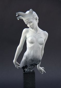 a white statue is standing on a black base and has her hands behind her head