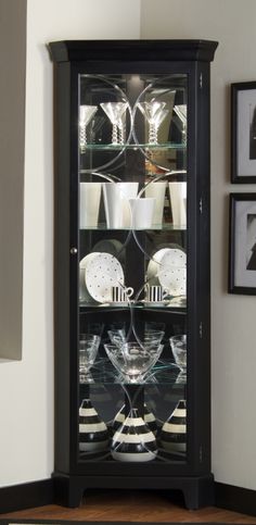 a glass cabinet with plates and cups in it next to pictures hanging on the wall