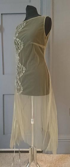 A very pretty 1920s over dress with a wonderful ethereal quality. One piece, a loosely fitted tunic in pale green net, sleeveless, with a high round neck at the front, low at the back. The dress falls to a handkerchief hem, and on the right hip there is a pleated panel, finished at the top with a long green silk ribbon tie / belt. Running down the front on the right side is beaded decoration, stylised deco floral.CONDITIONMostly good, there is one very small hole in the net, and the fabric is po Silk Dancing, Liquid Satin, Over Dress, Fitted Tunic, Deco Floral, Handkerchief Hem, Purple Velvet, Satin Skirt, Ribbon Tie