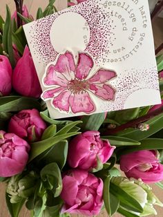 a bouquet of pink tulips sitting on top of a table next to a card