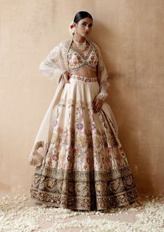 Editor's Note Presenting an opulent ivory raw silk lehenga set adorned with intricate floral thread embroidery and sumptuous velvet patchwork, elegantly highlighted with various embellishments. This captivating ensemble is paired with an embroidered blouse and dupatta, creating a regal and luxurious look perfect for grand occasions or elegant gatherings. The combination of the rich raw silk texture, the exquisite embroidery, and the ornate details on both the blouse and dupatta add a touch of op Motifs For Embroidery, Floral Embroidery Lehenga, White Wedding Lehenga, Ipl Videos, Sharara Style, Floral Thread Embroidery, Raw Silk Embroidery, Embroidery Lehenga, Velvet Patchwork