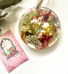 a glass bowl filled with flowers next to a plant and a card on a table