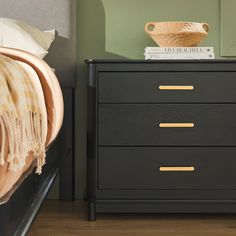 a black dresser with gold handles next to a bed