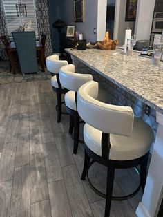 four white chairs sitting at a bar in a room with marble counter tops and flooring