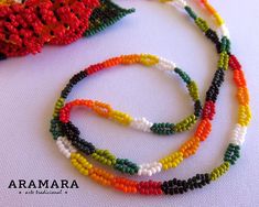 the beaded necklace is multicolored and has an orange, yellow, green, and red flower on it