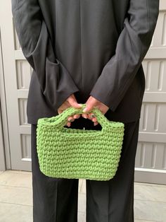 a person wearing a suit and holding a green crocheted purse in their hands