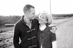 a man and woman standing next to each other on a dirt road in black and white