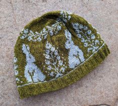 a green and white knitted hat sitting on top of a stone floor next to a rock