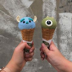 two people are holding ice cream cones with monsters on them, one is blue and the other is green