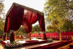 a stage set up for a wedding ceremony with red velvet drapes and white flowers