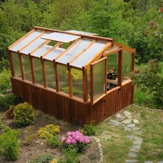 a small wooden greenhouse in the middle of a garden with flowers and trees around it