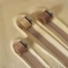 three jars of body lotion sitting on top of a white carpeted floor next to each other