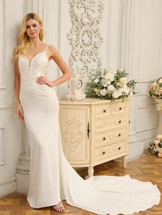 a woman in a white wedding dress standing next to a dresser with flowers on it