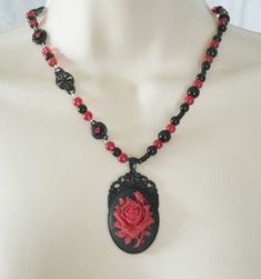 "Red Rose Necklace This beautiful necklace has red glass beads, black glass beads, seed beads, black metal connectors with rhinestones, black metal chain and a black metal pendant with resin rose. 20\" long. Lobster clasp." Gothic Beaded Jewelry Gift, Gothic Beaded Jewelry For Gift, Gothic Beaded Necklace For Gift, Gothic Black Bead Necklace For Gift, Gothic Black Beads Necklace For Gift, Gothic Black Beads Necklace For Jewelry Making, Handmade Gothic Beaded Necklaces With Round Beads, Ornate Handmade Red Necklace, Victorian Handmade Necklaces With Round Beads