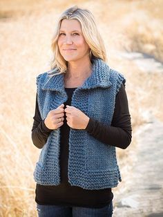 a woman standing in a field wearing a blue knitted sweater vest and black top