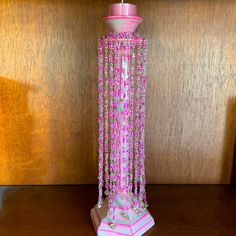 a pink candle with beads hanging from it's side on a wooden table next to a wall