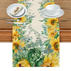 a place mat with sunflowers and green leaves on it, next to two white plates