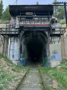 an old train tunnel with graffiti on the walls and tracks leading to it's entrance