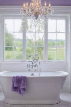 a white bath tub sitting under a window next to a chandelier and two windows