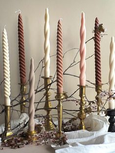 several candles are lined up next to each other on a white table with branches in the background