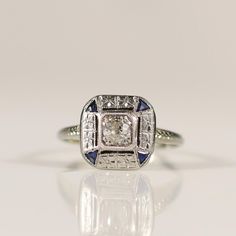 This Antique Art Deco ring captivates with its central diamond, flanked by four accent sapphires that add a touch of regal blue. The intricate filigree work showcases the meticulous craftsmanship typical of the Art Deco era, enhancing the ring's vintage allure. Delicately crafted, this ring is a timeless piece that embodies elegance and sophistication, perfect for any jewelry aficionado. Size: 6.5 Metal Type: 18K(Tested) Weight: 6.7G Width: 10.36mm Finger to Top of Ring: 4.94mm Hallmarks: 18k Gem Details:  Type: Diamond Cut: Old Mine Color: G-H Clarity: SI2 Carat: approx 0.25ct Accent Gems: Sapphire Quantity: 4 We look forward to providing you with an exceptional experience and helping you find more exquisite additions to your collection. *More Pictures Available on Request* R-624SPT-N65 Luxury Sapphire-colored Diamond Ring, Luxury Sapphire-colored Diamond Ring With Diamond Cut, Luxury Sapphire Diamond Ring With Diamond Cut, Luxury Sapphire Diamond Ring With Center Stone, Blue Platinum Art Deco Diamond Ring, Blue Diamond Art Deco Ring, Blue Art Deco Diamond Ring, Blue Platinum Jewelry With Single Cut Diamonds, Platinum Jewelry With Blue Single Cut Diamonds