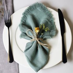 a white plate topped with a green napkin and two black forks next to a flower