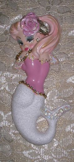 a pink and white mermaid figurine sitting on top of a bed