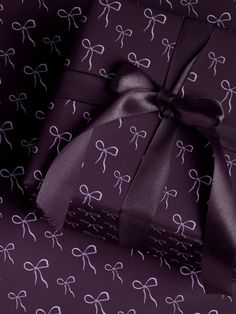 purple wrapping paper with white bows and ribbons on it, wrapped in dark purple ribbon