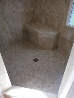 a tiled shower stall in a bathroom with white walls and tile flooring, along with a window