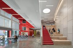 people are walking up and down the stairs in an open area with red walls, white ceilinging, and large windows