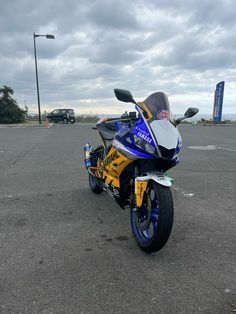 a blue and yellow motorcycle parked in a parking lot next to a street light on a cloudy day