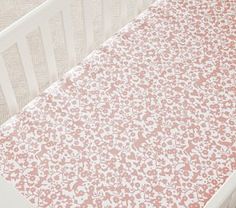 a baby crib with pink and white flowers on the bedding, next to a teddy bear