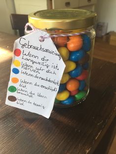 a jar filled with jelly beans sitting on top of a wooden table next to a tag