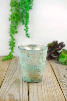 a green glass sitting on top of a wooden table next to some plants and greenery