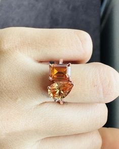 a woman's hand holding an orange and white ring with two diamonds on it