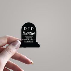 a person holding up a black and white tombstone shaped sticker that says rip twenties