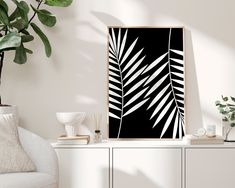 a black and white palm leaf print hanging on a wall next to a white chair