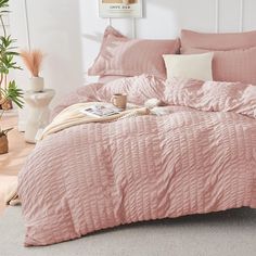 a bed with pink comforter and pillows in a room next to a potted plant