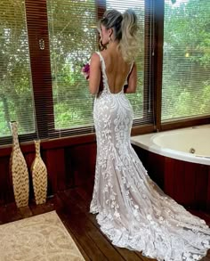 a woman standing in front of a bath tub wearing a wedding dress with an open back