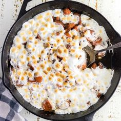 a skillet filled with food on top of a white tablecloth next to a blue and white checkered towel