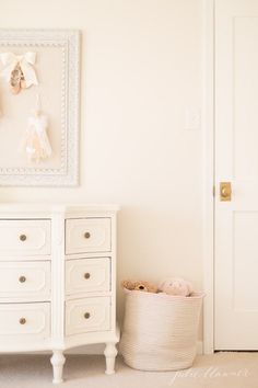 a white dresser sitting next to a white door in a room with a painting on the wall