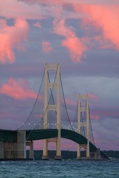 a bridge that is over some water with clouds in the back ground and pink sky behind it