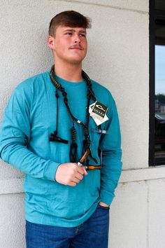 a young man standing next to a white wall holding a pen and wearing a necklace