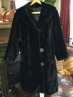 Made of thick, soft and plush faux fur, this coat is a classic shape with a unique v-shaped detail on the back of the collar. It has the original - very large! - buttons and two pockets. It is fully lined in a silky black fabric. The measurements, taken with the coat lying flat, are: shoulder to shoulder, 18 inches; armpit to armpit, 24 inches; sleeves, 22 inches; total length, 45 inches; bottom edge, 34 inches. In very good condition. Black Winter Vintage Outerwear, Vintage Black Winter Outerwear, Classic Black Fur Coat With Faux Fur Lining, Black Fur Coat Aesthetic, Black Vintage Fur Coat For Fall, Vintage Black Fur Coat For Fall, Vintage Long Coat In Faux Fur, Classic Black Fur Coat With Faux Fur Trim, Vintage Long Coat With Faux Fur Lining