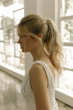 a woman standing in front of a window wearing a wedding dress and hair pinned into a low bun