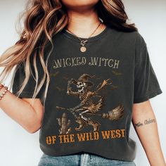 Ride into the spooky season with our "Wicked Witch of the Wild West" T-shirt, featuring a skeleton witch riding a broomstick. This unique design combines Halloween fun with a western twist, perfect for those who love both spooky and country vibes. Ideal for Halloween parties, fall festivals, or just showing off your wild and witchy spirit, this shirt is a must-have for your seasonal wardrobe. Made from soft, high-quality fabric, it ensures you stay comfortable while making a bold statement. Order your "Wicked Witch of the Wild West" shirt today and bring a touch of eerie adventure to your fall fashion! Production Time: 1-3 business days Shipping Time: 2-5 business days We GUARANTEE all of our products. If you are unhappy for any reason we do accept returns and exchanges for up to 30 days. Witchy Halloween T-shirt With Graphic Print, Halloween Band Merch T-shirt With Funny Print, Grunge Halloween Graphic Print Tops, Grunge Halloween Tops With Graphic Print, Grunge Graphic Print Tops For Halloween, Fall Witchy Graphic Print T-shirt, Halloween Distressed Graphic Tee, Grunge Halloween Pre-shrunk T-shirt, Halloween Graphic Tee Distressed T-shirt