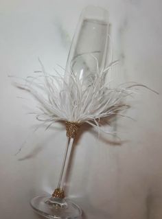 a glass vase with some white feathers in it and a gold beaded handle on the bottom