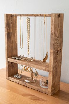 a wooden shelf with jewelry hanging from it's sides on top of a table