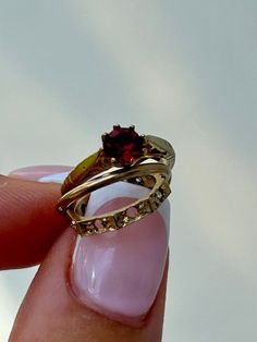 a woman's hand holding a gold ring with a red stone in the middle