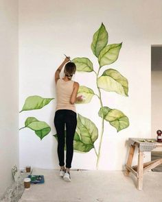 a woman is painting a plant on the wall